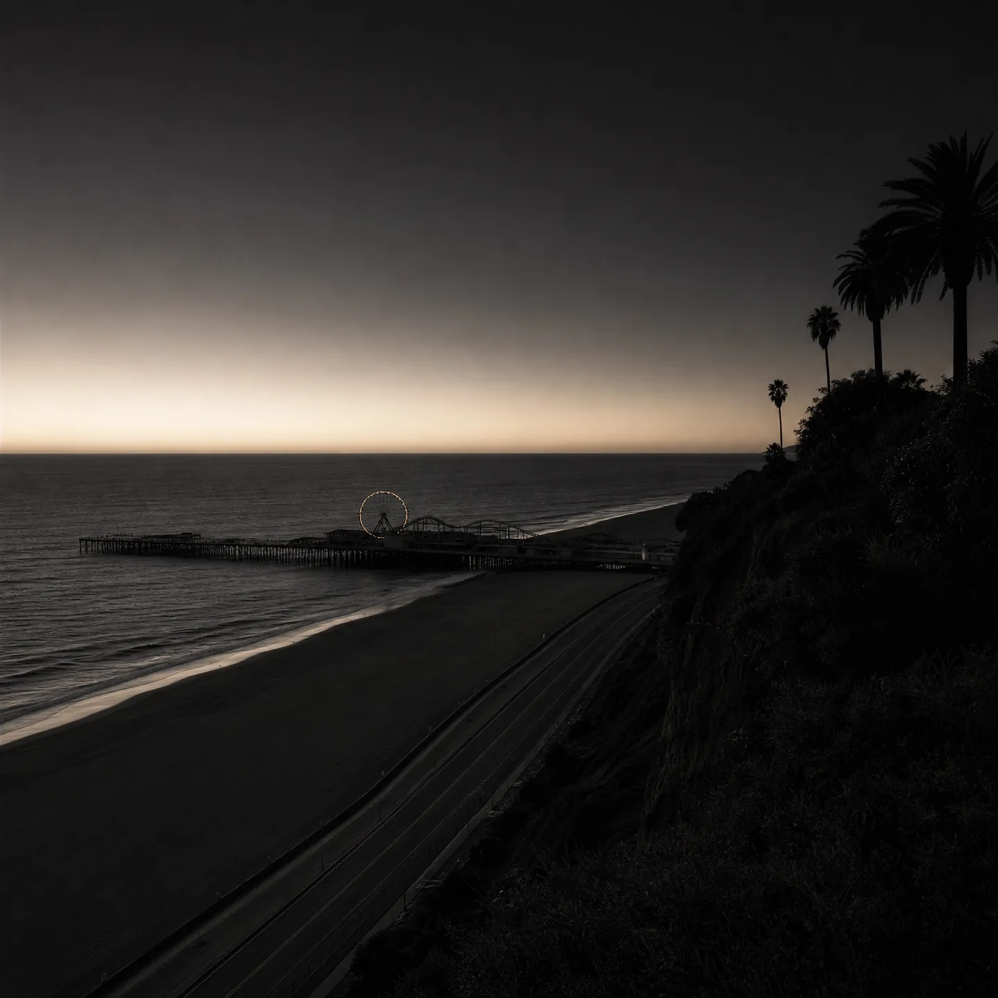 Santa Monica Pier and the Pacific Wheel extend into the bay below Palisades Park at blue hour.